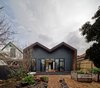 The extension sits on the property’s north side. Its zig-zag shape is a continuation (and reinterpretation) of the more traditional double hip roof of the existing house. The new construction combines Shadowclad boards, a Lysaght Longline steel roof, and Blackbutt eucalyptus decking. Photo of M House modern home