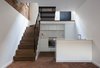 Modern home with Staircase, Metal Tread, and Wood Tread. The kitchen is situated in a sunken basement, underneath the staircase’s walnuts steps. The same joiner who built the house’s timber elements built the white cabinetry which are finished in a 40% gloss lacquer. Silestone countertops and integrated appliances maintain the space’s simple lines. Additional storage is fitted under the staircase. Photo 3 of Cleverly Stacked Floors Form a Roomy House On a Tight Lot