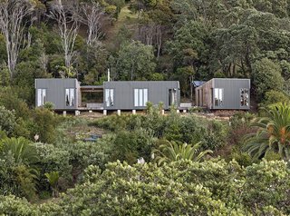 Located on the northern edge of Waiheke Island, approximately 800 feet from the nearest road, The Cora House sits atop a thicketed cliff that falls sharply into Hekerua Bayhe below. The prefab home's configuration maximizes views, while its siting limits environmental impact. Bonnifait + Giesen Atelierworkshop, the firm that designed the structure, was even able to retain the mature trees on the property.