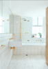 The bathroom was creatively composed using inexpensive Quarella Calacatta floor tiles, a Villery & Boch wall-mounted sink, and a Reece Sabine bath. Brass electroplated fixtures and FLOS Mini Glo Ball wall lights add a touch of sass to an otherwise understated space. Photo of A Tiny Apartment Renovation for a Growing Family in Melbourne modern home