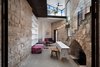 Modern home with Living Room, Bench, Shelves, Sofa, Storage, Pendant Lighting, Coffee Tables, and Concrete Floor. Warm and casual furniture is favored in the courtyard. Colorful seating, wood stools, and smart built-in shelving complete the space. The expandable table by Henkin Shavit is flanked by seven hanging pendant lights, symbolizing the branches of the Menorah. To the right of the table, the original stone arch leads to the home’s wine cellar. Photo of A 250-Year-Old Stone House in Israel with a Surprisingly Modern Interior