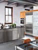 Modern home with Kitchen, Concrete Floor, Metal Counter, Metal Cabinet, Wood Cabinet, Refrigerator, Wall Oven, and Subway Tile Backsplashe. “The tile, with its sporadic bolts and nails, doesn’t need a lot of art, as it is art too,” Lisa says. “The copper windows... Well, you just can’t find those anymore.” Photo of Raw Materials Connect this Chicago Renovation with its Industrial Past