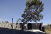 Modern home with Exterior, House, and Stone Siding Material. The house is built into the hillside but its top floor entrance is level with the street. The stone wall provides privacy while the garage and a pedestrian walkway—seen exact center, by the tree—bridge the gap. Photo of A Daring Hillside Home Made of Wood, Concrete, and Volcanic Stone