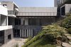 Modern home with Outdoor, Boulders, and Walkways. A stone path leads from the backyard, up the hillside, and arrives at the streetside entryway. The rhythmic pattern of the concrete garage, as well as the pedestrian walkway, are front and center. The privacy of the living and sleeping areas, seen at the left through floor-to-ceiling windows, are shielded from public view by the hill and the stone wall. Photo of A Daring Hillside Home Made of Wood, Concrete, and Volcanic Stone