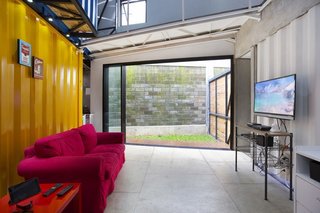 A sliding glass door in the downstairs living room leads to an outdoor patio and green space. A sofa and side table from IKEA complement an unfinished wood entertainment center.