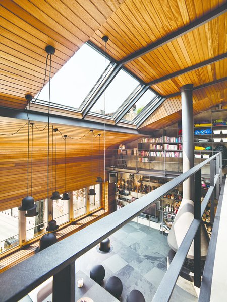 Structural changes were immediately made to the original shell to bring in more natural light. The small windows on the front façade were dramatically replaced with a folding window assembly that stretches the entire width of the room. Skylights were cleverly added slightly beneath the peak pitch of the roof to funnel light towards the mezzanine, while still illuminating the main floor below. Warm, rich iroko wood spans the ceiling and wall, and also extends to the seating bench beneath the window.