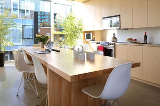 The kitchen features stainless steel prep counters, a Samsung stove, and Panasonic over-the-range microwave. The room is bordered by two full walls of windows, allowing light to flood the space at all times of the day. A custom birch butcher block table furnishes the family gathering space.