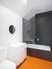 Low-maintenance, sustainable materials were favored throughout the house. Striking orange Pirelli studded rubber floors were chosen for the main bathroom. Clean white fixtures and black shower cladding complete the graphic space. Photo 5 of 1850s Prefab Cottage from Boston Finds New Life in Australia modern home