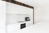 Black Electrolux induction cooktop and electric oven offer graphic contrast to the minimal white Corian counters and white cabinetry in the home’s kitchen. Photo 9 of 1850s Prefab Cottage from Boston Finds New Life in Australia modern home