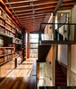 Suspended over the living room, the library bridge connects the second floor rooms of the house. The transitional space contains built-ins and desks where the owners and their three-year-old daughter can sit and read. The steel of the staircase is supported entirely by the adjacent concrete wall. A marriage of concrete, wood, and glass is used in the space, and the large windows let light in and offer a view of the roof garden. Photo 8 of Hybrid Home modern home