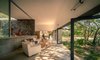 The home’s living room flows seamlessly into the outdoors. Mineral materials that were locally sourced and crafted were favored throughout the home. Polished concrete floors, natural basaltic walls, and white interior walls made of cement and lime plaster carry through the home. Aluminum-framed sliding doors separate the living room from the central patio. Traditional Mexican furnishings complete the space. Photo of This Super Green Home in Mexico Embraces Nature Through Huge Pivoting Glass Doors modern home