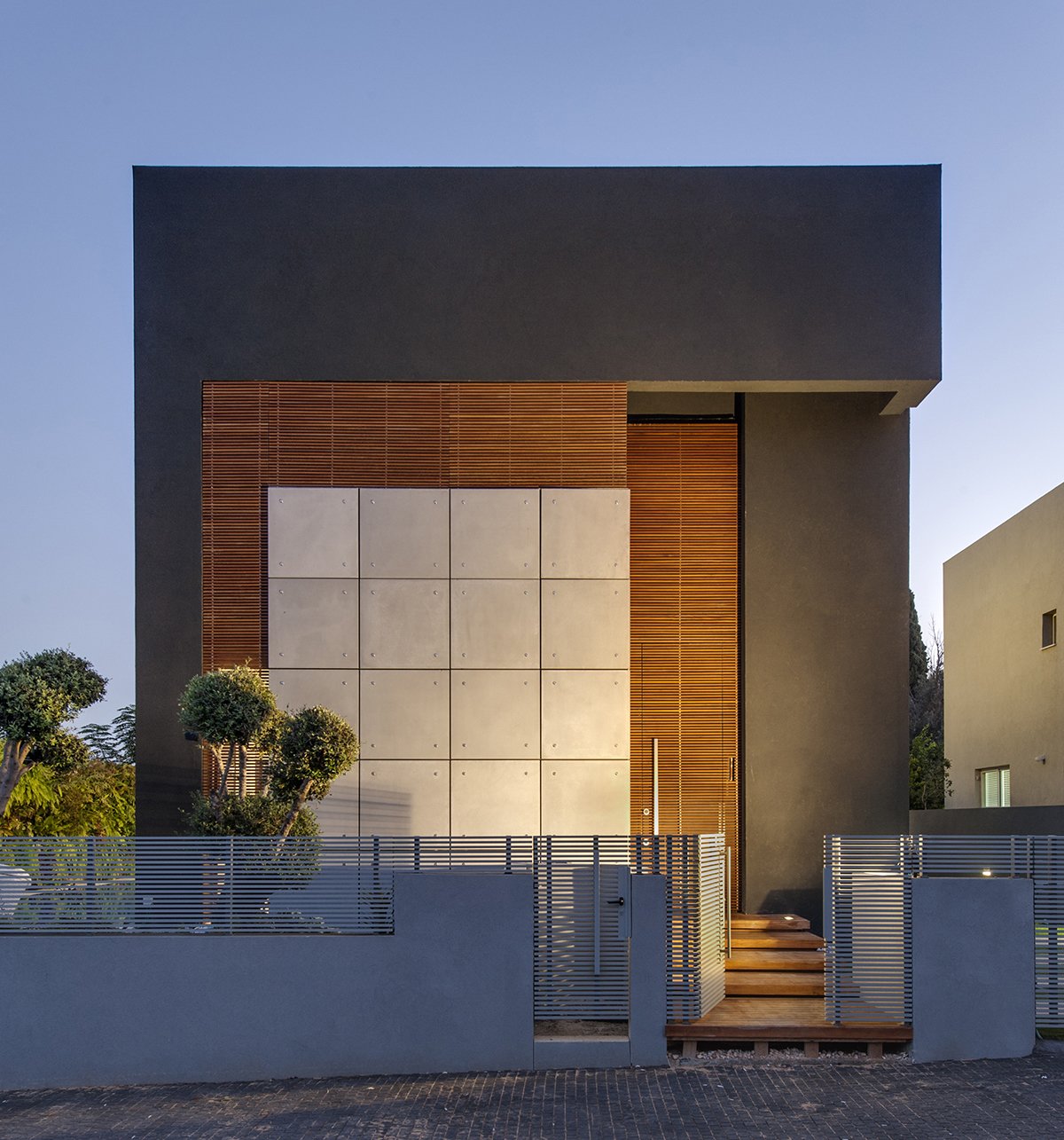 The home’s facade is private and mysterious, without discernable windows or openings. The exterior is made of concrete tiles, black plaster, and wooden trellises. The trellises act as a light screen, allowing only cracks of light to penetrate the exterior. The entry is camouflaged in the plane of the trellises, which adds to the opaque and impenetrable aesthetic at the front facade.