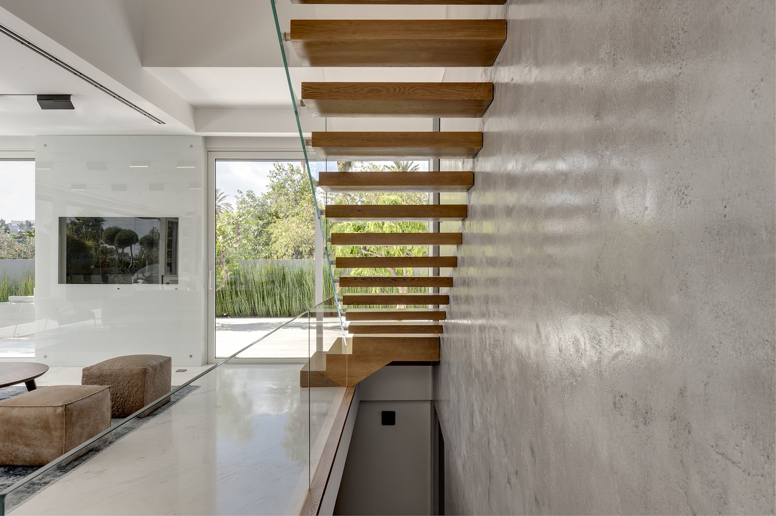 Inside, the home immediately opens up with light and natural views. The cantilevered stairs leading to the first floor offer a dramatic focal point. The stairs, wrapped in natural oak, are anchored to the exposed concrete walls on one side, and bordered by a clear glass railing on the opposite side.