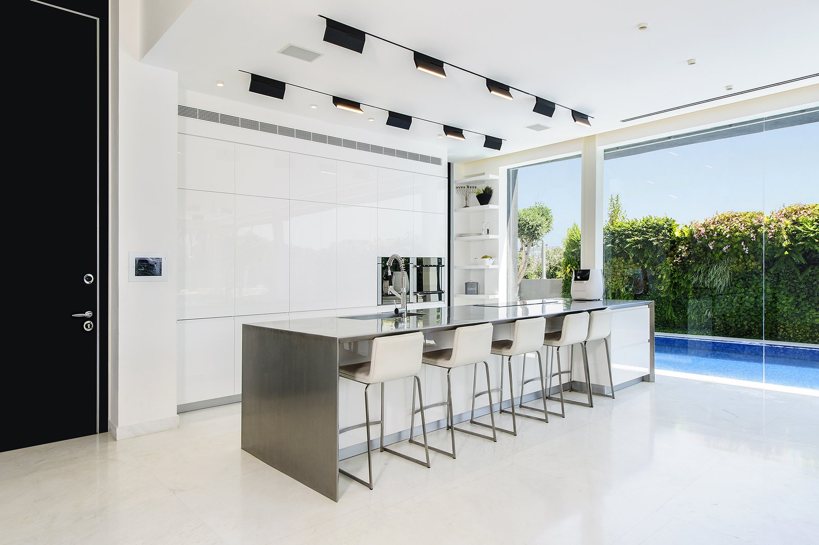 A well-lit and open ground floor with a strong interior-exterior connection was at the top of the family’s wish list. The kitchen makes the most of a compact space through its intimate relationship with the adjacent pool and public outdoor space. The spaces features hardware-free white cabinets and a stainless steel center island. The white kitchen floors provide visual continuity with the white pavement directly outside.