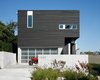 “The house turns its back to the street while opening up to the views to the northeast through a large glazed corner window system,” Hutchison says. One-by-four and one-by-six inch cedar siding, which were pre-stained in Cabot Semi-Transparent Black, were placed vertically and horizontally on the exterior as a subtle detail. Photo of Portage Bay Bungalow modern home