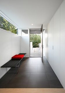 "A series of stepped concrete site walls lead you gradually up to a covered exterior entry, which opens onto a compressed entry foyer," Hutchison says. A Bertoia bench by Knoll sits in an entryway covered by Mosa’s Greys Collection tiles.