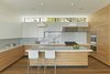 Modern home with Kitchen, Engineered Quartz Counter, White Cabinet, Medium Hardwood Floor, Glass Tile Backsplashe, Recessed Lighting, Pendant Lighting, Wall Oven, Range, and Range Hood. The architects wanted to create as much of a buffer as possible against the urban traffic outside the kitchen. A clerestory window manages to maintain a visual connection with the neighborhood while blocking its noise. The kitchen features Pleat Box pendant lights from Marset and Lio Stools by Roberto Barbieri for Zanotta. Photo 2 of Noe Residence