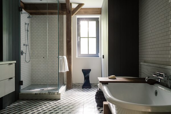 In the master bathroom, the cement floor tiles are by Mosaic House; the glazed subway tiles are from Daltile; and the trim is honed, vein-cut Montclair Danby marble. The Signature Hardware tub sits in a custom wood cradle designed to match the home’s timber frame; the fixtures are by Waterworks. The Twist stool is from Classic Country in nearby Hudson, New York.