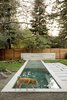 Modern home with Outdoor, Small Pools, Tubs, Shower, Lap Pools, Tubs, Shower, and Back Yard. Sphinx, the family Carolina dog, scouts the perimeter of the Concrete Collaborative pavers in the backyard. The pavers were installed on a slight angle to channel water to the surrounding gravel, lawn, and planting beds. This substantially lowers the landscape's water demand. Perforated PVC pipes and a pump move excess rainfall (which would otherwise go to storm drains) into an underground basin where it can later drain off. Redwood fencing reflects the material palette of the interior and creates visual continuity around the backyard. Photo of A Couple Puts Their California Home on Track for LEED Certification