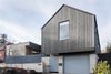 The cedar-clad front facade features one of the home’s defining design elements: a cantilevered gable that appears to float over the garage. The project is composed of two unique forms, divergent in convention but complementary in execution. A traditional gable, simplified and modernized, sits next to a striking modernist cube. A custom entry gate fabricated by Dovetail’s metal shop and a steel privacy fence add color to the front elevation. Photo of Central District Residence modern home