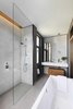 Modern home with Bath Room, Freestanding Tub, Full Shower, and Marble Counter. The adjoining master bathroom is connected by mirrored pocket door with bronze trim at the frame. The graphic space features a Kaldewei tub, Domus tiles, and Dornbracht faucets and fixtures. A marble vanity top and medicine cabinet sit against the far wall; a compact wood bench slides smartly under the vanity. Photo of Brass Is Everywhere at this Classical-Meets-Modern Flat in London