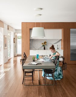 The firm collaborated with Kountry Kraft and its modular manufacturer, Simplex Homes, to expand the palette of materials, including the teak cabinetry used in the kitchen and dining areas. Interior designer David Bentheim suggested the marble backsplash for the bar area. Antique dining chairs, an LED Aurea pendant lamp by FontanaArte, and a Paolo Piva table from B&B Italia complete the room.