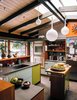 Modern home with Kitchen, Undermount Sink, Wall Oven, Cooktops, Refrigerator, Wood Counter, Colorful Cabinet, Concrete Floor, Ceiling Lighting, and Pendant Lighting. "Maintaining sight lines to the outdoors and the adjacent den, we introduced a connectivity that transforms the kitchen into the center of family life, Photo 3 of Modernist Gem Revival