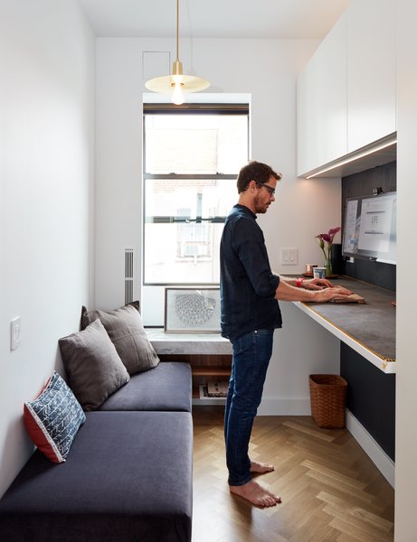 Standing room only! If you're in need of home office ideas for small spaces, consider a fold-down desk that allows you to stand while working. This one, a New Table Concept by Resource Furniture, is a great option. Comfortable seating, ample storage, and a modern light fixture round out the space.