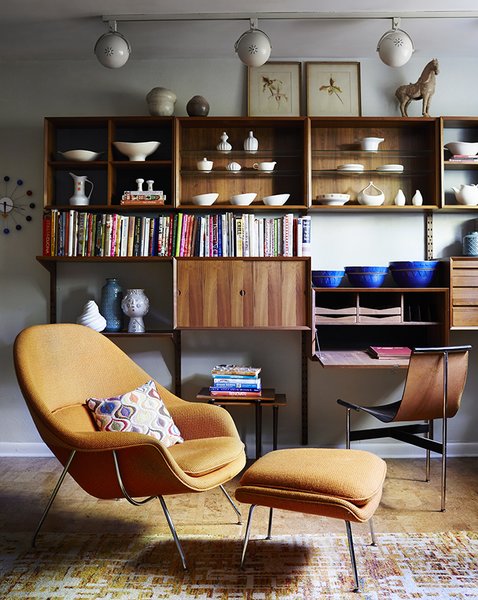 Illuminated by track lighting, a teak wall unit by Poul Cadovius showcases pottery by Eva Zeisel and Paul McCobb, among others. The desk seat is a T chair by William Katavolos, Ross Littell, and Douglas Kelley; the Womb chair is by Eero Saarinen for Knoll.