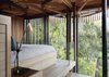 Modern home with Bedroom, Table Lighting, Light Hardwood Floor, and Bed. Lofted amid eucalyptus and oak trees, Graham Paarman’s house in South Africa is a glassed-in, steel-frame structure with a veil of vertical slats. Excluding outdoor areas, it measures about 720 square feet. Half-round bays project to form a balcony, a pergola, a dining alcove, and a bathroom. Photo 7 of Paarman Tree Home