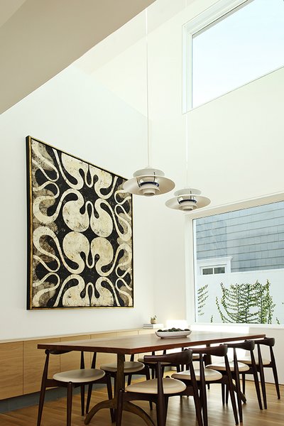 The home’s open-floor plan combines the dining and living areas into a shared space. The dining table is a custom walnut plank top with a base by Organic Modernism. It is surrounded by CH20 Elbow chairs by Hans J. Wegner for Carl Hansen &amp; Son.