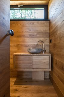 The wood-clad bathroom features a full shower and custom-made natural stone sink, which was created from a rock found at a neighboring river. 