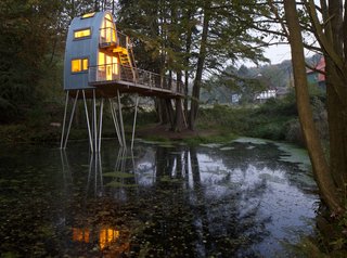 A stately group of hemlock trees on the shore of two ponds provided the perfect site for this enchanting, two-story structure located in Uslar, Germany. Designed for a client's young son, the tree house features a rounded steel facade with flanking wooden arches built from laminated wood.