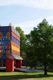 Resting on four huge red cylinders, the multi-colored structure encompasses a central arena where visitors can view the structure from numerous perspectives. 