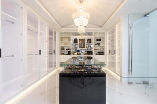 A glamorous walk-in closet is fitted with marble floors and custom-built cabinetry and shelving. 