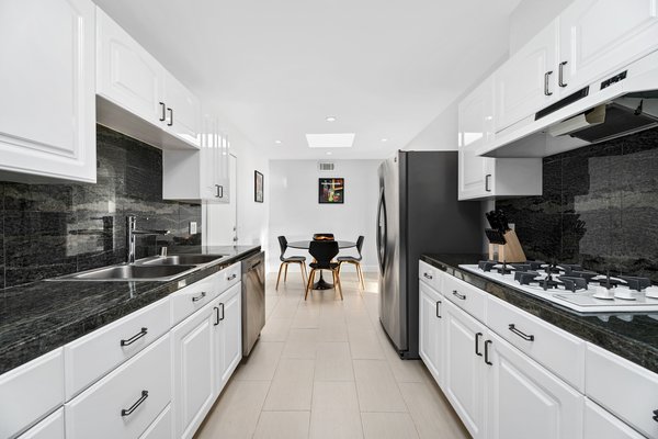 The galley kitchen features crisp white cabinetry with contrasting black accents.