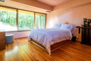 Plays on different forms and shades of natural light continue throughout the two-bedroom home. This bedroom offers a wall of windows and raised ceilings.
