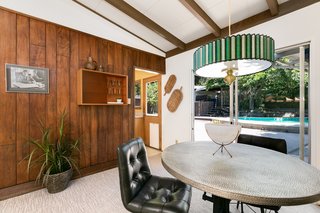 The dining room faces a large glass door with views of the swimming pool and patio. An original lighting fixture hangs above the table.