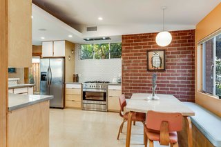 The updated kitchen features custom maple and plywood cabinets built to resemble the original space. An exposed brick wall and triangular backsplash tiles further accent the modern design.