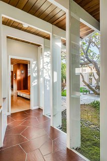 On the opposite side of the home, a hallway leads to the master bedroom. The staggered wall of glass appears to follow a geometric pattern established by the slate floors.