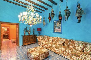 The formal sitting area is painted in a striking shade of sky blue. Antiques line the walls and hang from the timber-beamed ceilings, while a different majolica tile motif covers the floor.