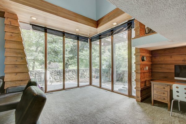 Clapboard walls in the living room meet up with a large glass wall in the corner. Overlooking a stone-walled patio, the large windows enhance the room's relationship with the outdoors.