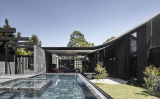 The home's sloping roofline sweeps upward from an enclosed courtyard. The character of the house changes as light hits the mix of materials—from rough stone to sleek black aluminum—throughout the day, giving it a sense of constant motion.