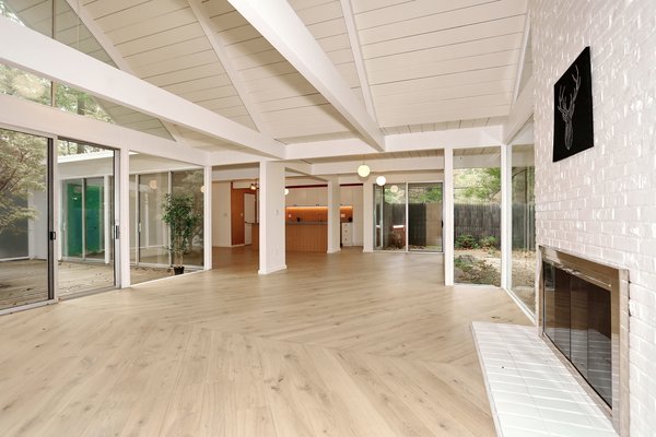 Glass walls encapsulate the open-plan living room, which rests directly under the home's double A-frame roof. The exposed beams, ceilings, and fireplace were painted a crisp white as part of the renovation. Wide-plank, herringbone-patterned floors were also laid throughout.