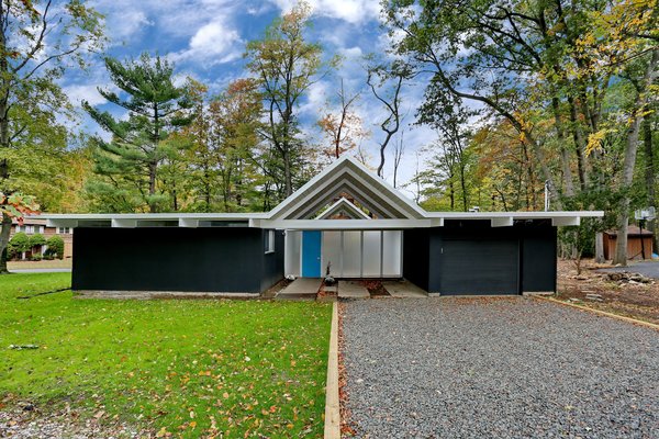 The 1962 midcentury at 130 Grotke Road is conveniently located just a short drive from Manhattan. A bright blue door pops amidst the home&rsquo;s black exterior siding.