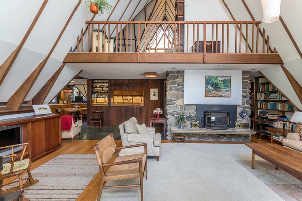 The home’s main living area features cathedral ceilings and a large loft overhead. The space is divided by a stone fireplace and built-ins that lead to the kitchen.