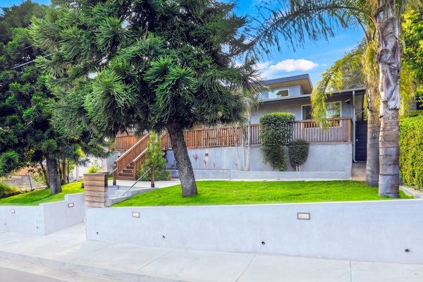 The front facade is unassuming, shielded by large star pine trees. A series of steps lead up to a large front deck and the main entrance.