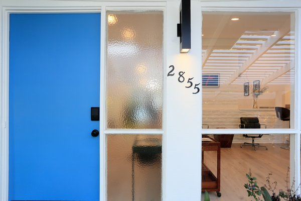 Shaded by a pergola, the sky blue front door stand alongside full-height textured and transparent glass windows.