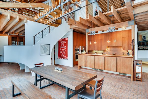 The double-height space features expansive public areas along the ground floor, with original brick and wood details throughout. A dining area is open to the kitchen in the corner while a staircase curves around while leading to a catwalk upstairs.