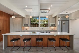 Kitchen, Engineered Quartz Counter, Vinyl Floor, Ceiling Lighting, White Cabinet, Pendant Lighting, Stone Slab Backsplashe, and Undermount Sink A 14-foot-long island topped with quartz offers bar seating in the kitchen. Light wood cabinetry and built-in Gaggenau appliances round out the space.